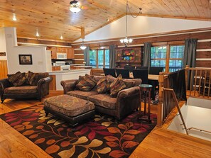 A cozy cabin interior with a wooden ceiling, a dining area, and a living room furnished with leather couches and a patterned rug. - Peaceful log cabin on large acreage with fire pit and private hiking trails. (Nashville)