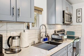 A modern kitchen with grey cabinets, a stainless steel kettle, a coffee maker, a toaster, and a microwave. - Burien Modern Cozy - Near Airport & Amenities (Burien)