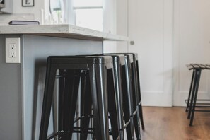 Una cocina con encimera blanca, un enchufe y taburetes negros.