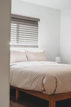 A bedroom with a bed, a window with blinds, and a bedside lamp. - Burien Modern Cozy - Near Airport & Amenities (Burien)