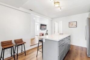 A modern kitchen with a large island, wooden bar stools, and a stainless steel refrigerator. - Tranquil Burien Cozy - Near Airport & Amenities (Burien)