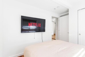 A bedroom with a bed, a wall-mounted TV displaying 'NETFLIX,' and a white door. - Tranquil Burien Cozy - Near Airport & Amenities (Burien)