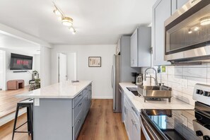 A modern kitchen with a large island, stainless steel appliances, and a flat-screen TV displaying 'NETFLIX'. - Tranquil Burien Cozy - Near Airport & Amenities (Burien)