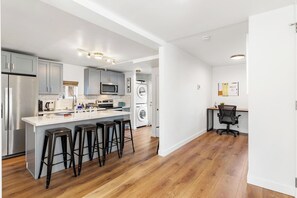 Une cuisine moderne dotée d’un îlot central, de tabourets de bar, d’un lave-linge et d’un espace aménagé en bureau.