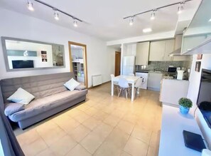 A modern living room with a sofa, a dining table, and a kitchen area. - Apartment with a pool near the beach (Sant Feliu de Guíxols)