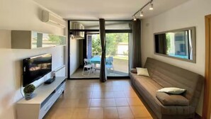 A modern living room with a flat-screen TV, a sofa, and a dining area with chairs. - Apartment with a pool near the beach (Sant Feliu de Guíxols)
