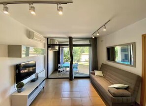 A modern living room with a flat-screen TV, a sofa, and a dining area with chairs. - Apartment with a pool near the beach (Sant Feliu de Guíxols)