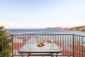 Ein Balkon mit Tisch für zwei Personen, mit Blick auf die Küste und einen klaren Himmel.