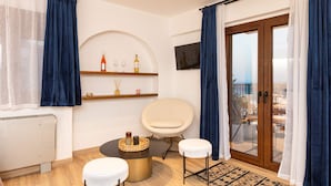 A modern living room with a round table, two white stools, a television mounted on the wall, and a balcony with a view. - Studio Tepes - Natassa Samos Seaview Balcony Suite (Samos)