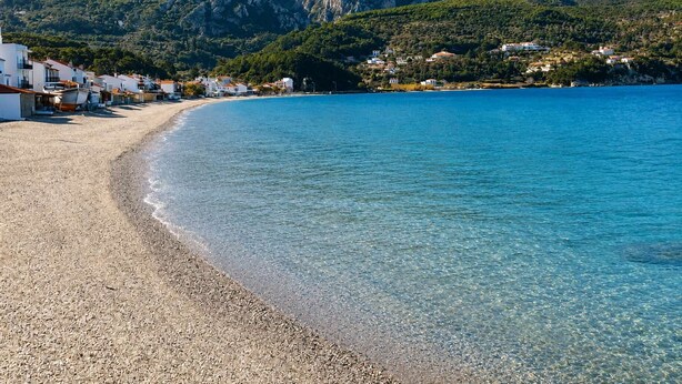 A coastal beach with pebbly shore, clear blue water, and houses along the coastline. - Studio Tepes - Natassa Samos Seaview Balcony Suite (Samos)