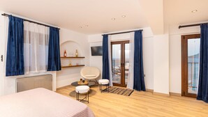 A modern bedroom with a bed, a chair, a small table, and a TV. - Studio Tepes - Natassa Samos Seaview Balcony Suite (Samos)