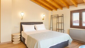 A bedroom with a bed, wooden ceiling beams, wall-mounted light fixtures, a window with a view, and a metal rack against the wall. - Studio Tepes - Velis Samos Sea View Balcony Suite (Samos)