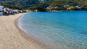 A coastal town with a pebble beach, clear blue waters, and mountainous backdrop. - Studio Tepes - Velis Samos Sea View Balcony Suite (Samos)