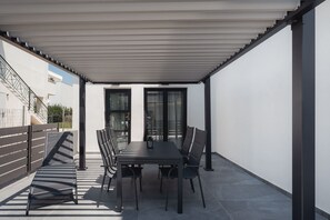 Eine überdachte Terrasse im Freien mit Tisch, Stühlen, einer Brüstung und Blick auf die Straße.