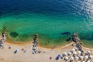 Ein Strand mit klarem Wasser, darin schwimmende Menschen und Sonnenschirme.