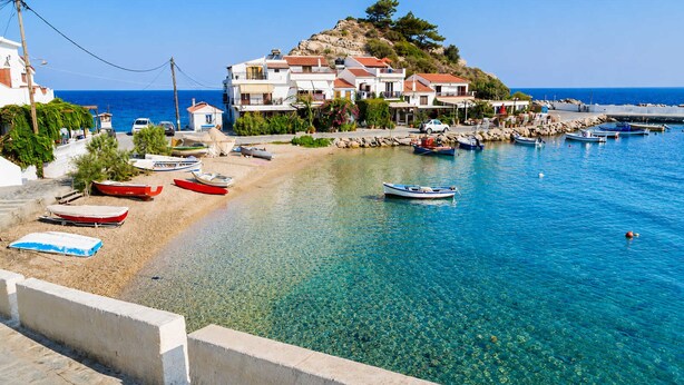 A coastal town with clear blue waters, boats on the shore, and buildings with red roofs. - Studio Tepes - Samos Sea View Balcony Suites (Samos)