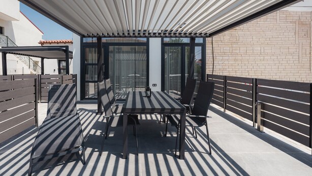 An outdoor patio with a table and chairs, a pergola, and a glass enclosure. - Chalkidiki Peaceful Retreat With Private Parking (Sithonia)