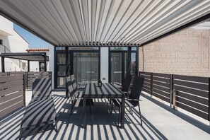 An outdoor patio with a table and chairs, a pergola, and a glass enclosure. - Chalkidiki Peaceful Retreat With Private Parking (Sithonia)