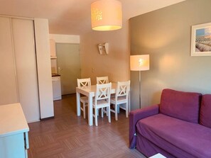A room with a dining table and chairs, a purple sofa, and a wall-mounted lamp. - Appartement 3 étoiles - Piscine  - ccbgfca (Gréoux-les-Bains)
