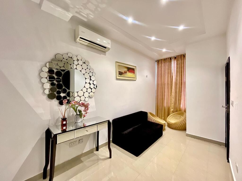 Una sala moderna con un espejo redondo, un sofá negro, una consola y una silla de mimbre.
