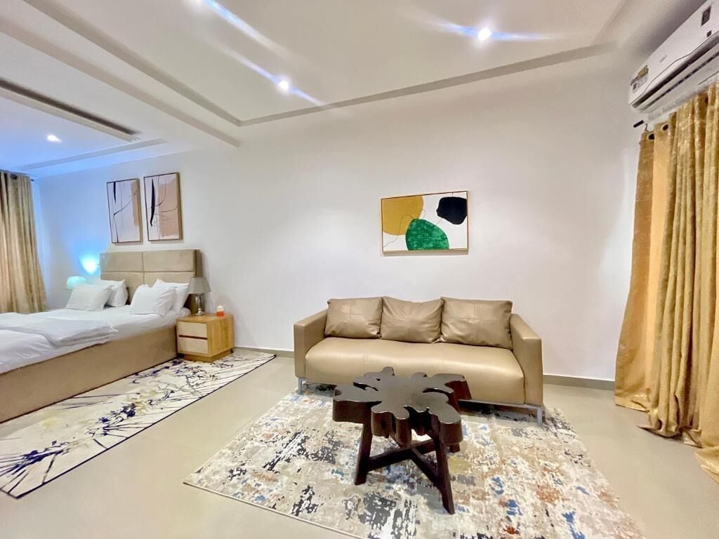 Una habitación de hotel moderna con cama, sofá, mesa de centro y un cuadro en la pared.