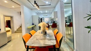 Un comedor moderno con una mesa de mármol y sillas color naranja, una escalera que conduce a otra habitación, y una cocina al fondo.