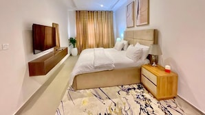 Habitación de hotel con cama, mesita de noche, lámpara y televisor de pantalla plana montado en la pared.