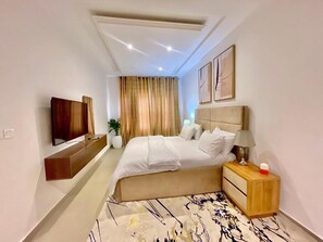 A hotel room with a bed, bedside table, lamp, and a flat-screen TV mounted on the wall.