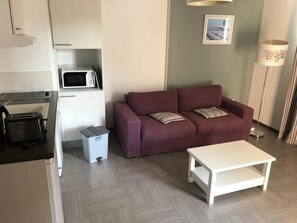Ett kompakt bostadsutrymme med ett litet kök, en soffa, ett soffbord och en lampa.
