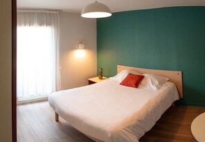 Une chambre à coucher avec un lit, une table de chevet, une lampe et une fenêtre avec des rideaux.