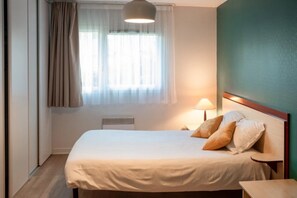 A hotel room with a bed, a bedside lamp, a window with curtains, and a radiator. - Appartement 2 étoiles - ccbgffd (Brest)