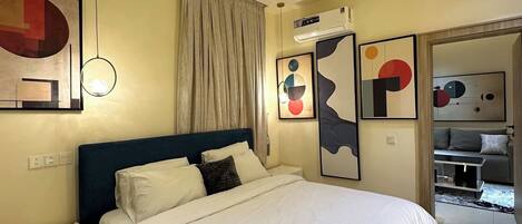 Habitación de hotel con cama, mesita de noche, silla, aire acondicionado instalado en la pared y arte abstracto en las paredes.