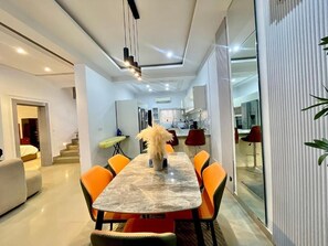 A modern dining area with a marble table and orange chairs, a staircase leading to another room, and a kitchen in the background. - CALMDAY COURT (Federal Capital Territory)