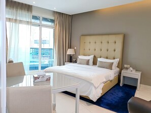 A hotel room with a large bed, a desk, a chair, a nightstand, and a view of the city. - Iconic Waterside Studio  Near Dubai Mall (Dubai)