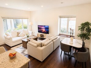 Ein modernes Wohnzimmer mit einer Sofagarnitur, einem Fernseher und einem Essbereich mit Tisch und Stühlen.