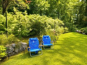 Zwei blaue Liegestühle auf einer gepflegten Rasenfläche mit einer Hecke und einer Steinmauer.
