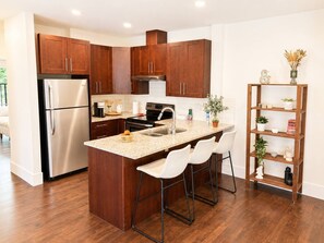Eine moderne Küche mit Holzschränken, Edelstahlgeräten, einer Granitarbeitsplatte und einer Bar mit Barhocker.