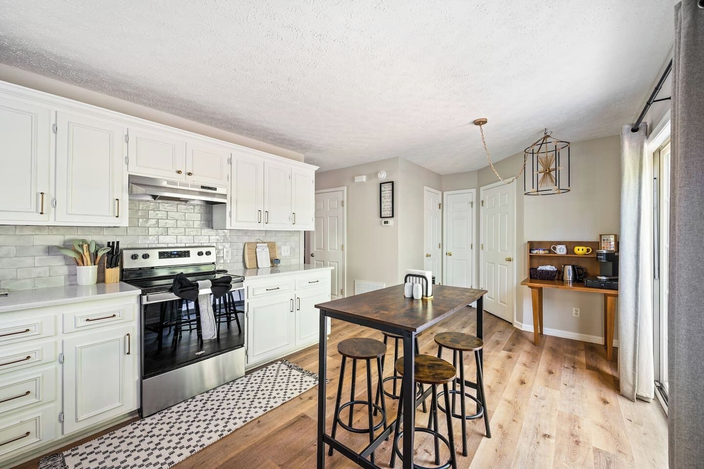 Une cuisine moderne avec des meubles blancs, un îlot central doté de tabourets, un four encastré et un luminaire suspendu.