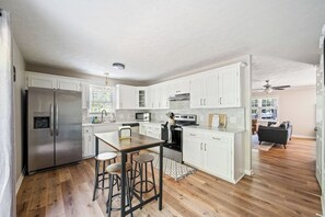 A modern kitchen with white cabinetry, stainless steel appliances, and a dining area with stools.