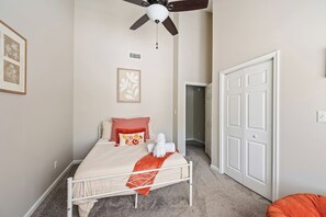 A bedroom with a bed, a ceiling fan, a door, and a carpeted floor.
