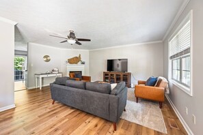 A spacious living room with hardwood flooring, a gray sectional sofa, a wooden entertainment center, and a flat-screen TV.
