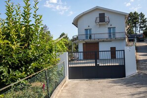 Ein zweistöckiges Haus mit Balkon, befestigter Auffahrt und einem Zaun aus Maschendraht.