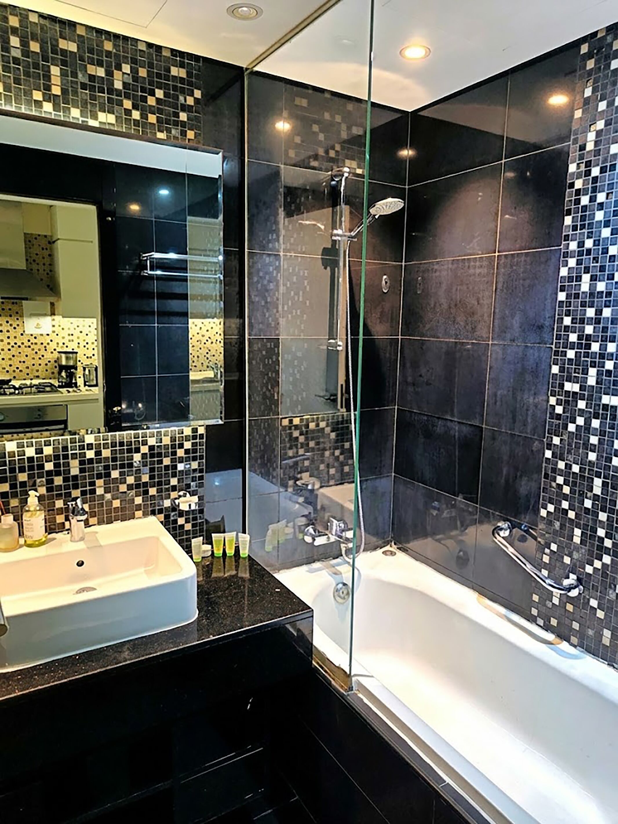 A modern bathroom with a glass-enclosed shower, a white bathtub, and a black tiled backsplash.