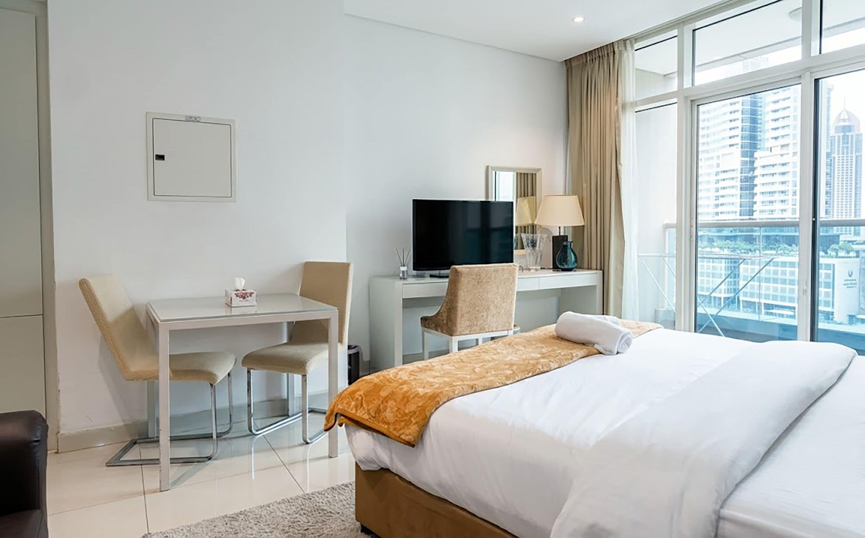 Une chambre d’hôtel équipée d’un lit, d’un bureau, d’une chaise, d’une télévision et d’une fenêtre donnant sur la ville.