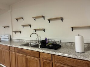 A kitchen with a granite countertop, a stainless steel sink, wooden cabinets, and multiple wall-mounted shelves. - A Tranquil country home near Ratcliff State Park (Kennard)