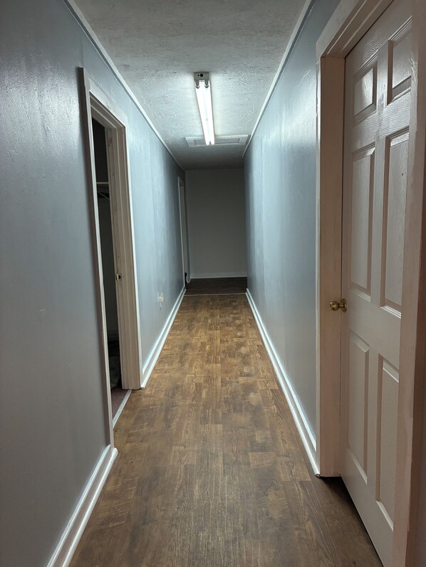 A hallway with a wooden floor, white walls, and a door on the right.