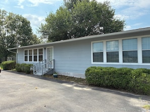 A single-story building with a covered porch, a staircase, and a row of windows.