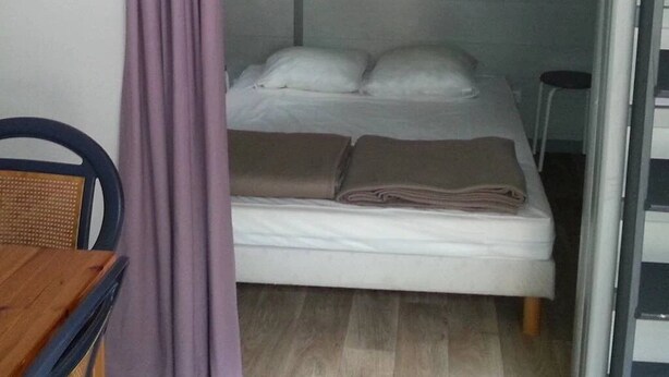 A single bed with a headboard, a small table, and a chair in a room with a curtain.