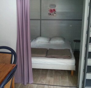 A single bed with a headboard, a small table, and a chair in a room with a curtain.