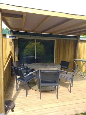 An outdoor wooden deck with a round table and chairs, a covered area, and a cat on the deck.